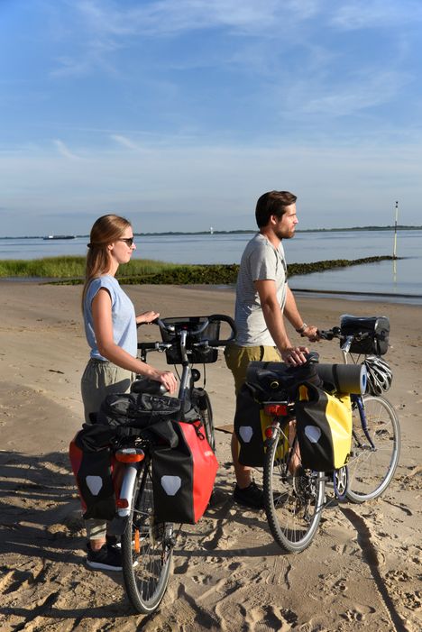 Paar ist auf dem Elberadweg unterwegs, macht eine Pause am Elbstrand in Brokdorf und genießt den Blick aufs Wasser.