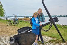 Paar macht auf seiner Radtour in Wedel am Schulauer Hafen eine Pause. An einem alten Anker schauen sie in eine Radkarte