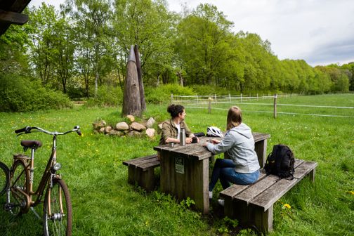 Paar ist auf dem Radfernweg Ochsenweg unterwegs und genießt eine Pause auf einem Hörnerplatz mit Blick in die Natur.