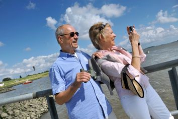 Paar steht am Wasser und fotografiert die Umgebung