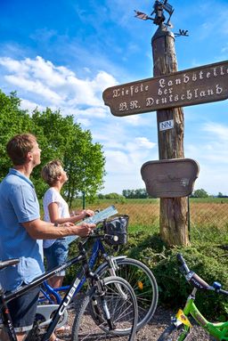 Eine Familie ist mit dem Rad unterwegs auf dem Land-unter-Törn und macht Pause an der Tiefsten Landstelle Deutschlands.