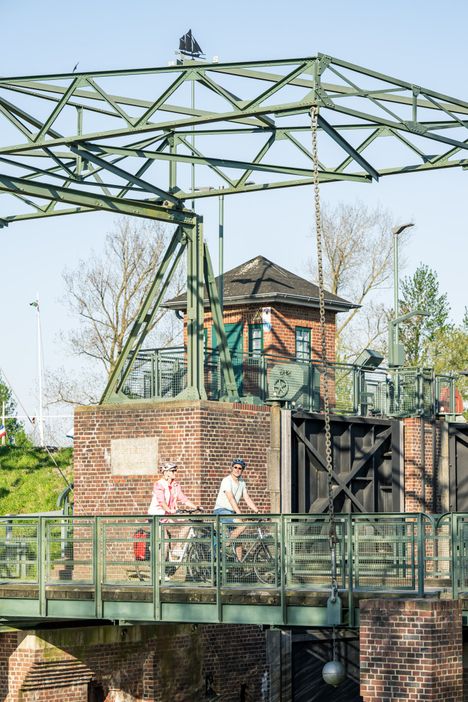 Ein Paar ist auf dem Mönchsweg unterwegs und passiert gerade die historische Schleuse Kasenort, die die Stör und die Wilsterau verbindet.