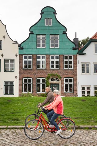 Paar fährt mit dem Fahrrad an der historischen Hafenzeile in Glückstadt entlang.