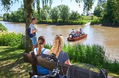 Eine kleine Gruppe mit drei jungen Erwachsenen wartet am Ufer der Krückau auf die Fähre Kronsnest. Kreis Steinburg, Kreis Pinneberg