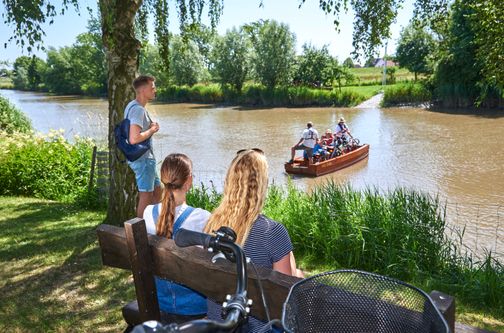 Eine kleine Gruppe mit drei jungen Erwachsenen wartet am Ufer der Krückau auf die Fähre Kronsnest. Kreis Steinburg, Kreis Pinneberg