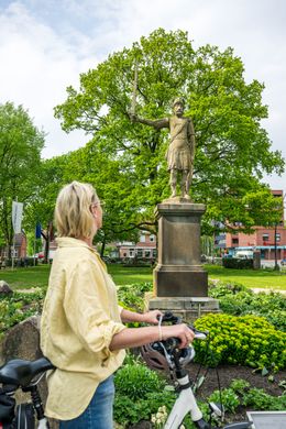 Eine Frau ist mit ihrem Fahrrad in Bad Bramstedt unterwegs und schiebt ihr Rad an der Roland-Statue vorbei.