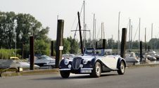 Oldtimer fährt am Haseldorfer Hafen entlang. Im Hintergrund sind Segelschiffe und Boote zu sehen.