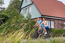 Paar fährt mit dem Fahrrad durch die Elbmarschen. Im Hintergrund steht ein altes rotes Backsteinhaus.