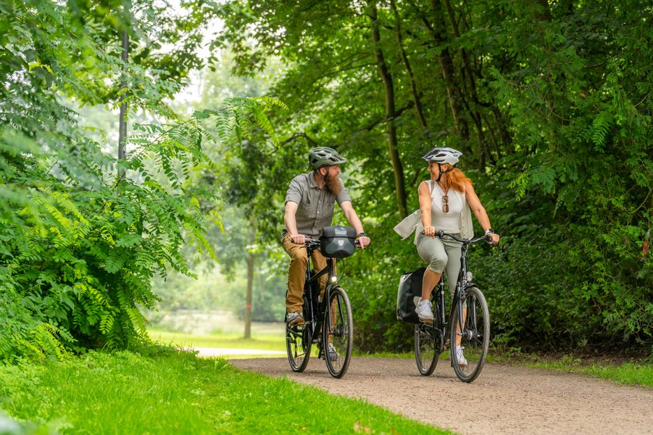 Paar genießt eine Fahrradtour im Grünen und fährt durch den Kurpark in Bad Bramstedt.