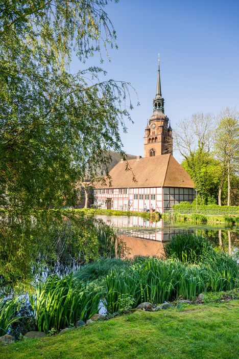 Blick auf die kleine idyllische Parkanlage mit Teich im Klosterhof Itzehoe. Im Hintergrund ragt der Kirchturm von St. Laurentii in den Himmel.