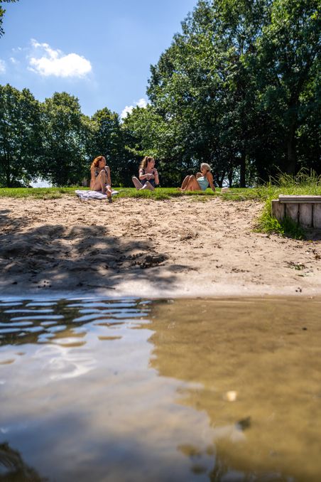 Drei Freundinnen entspannen sich am Wasser und liegen in der Sonne. 