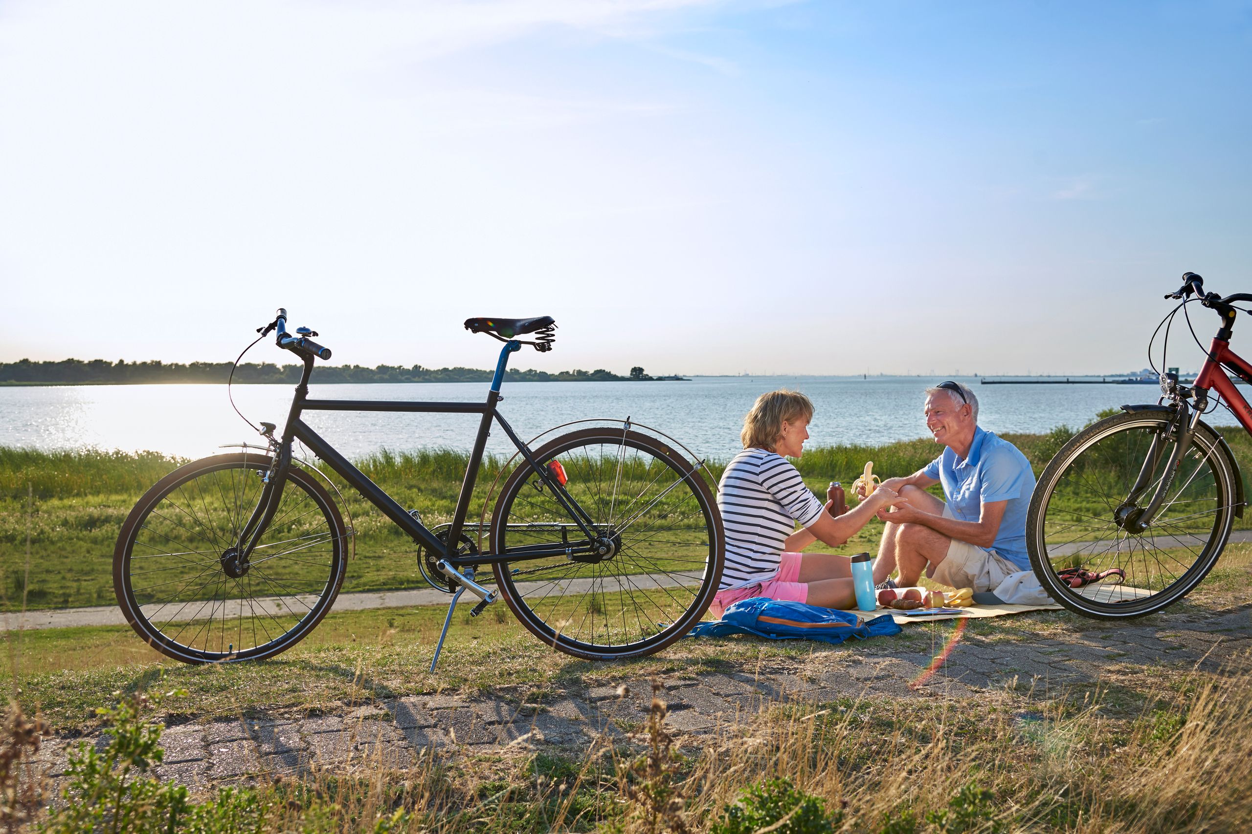 Paar ist auf Fahrrädern an der Elbe unterwegs und macht auf dem Deich eine Pause mit Picknick.