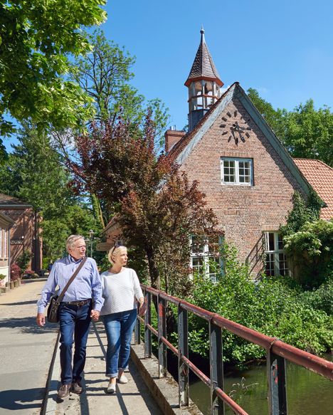 Ein Ehepaar spaziert über die Brücke zur Schlossinsel im Rantzauer See in Barmstedt. Im Hintergrund steht das Schlossgefängnis.