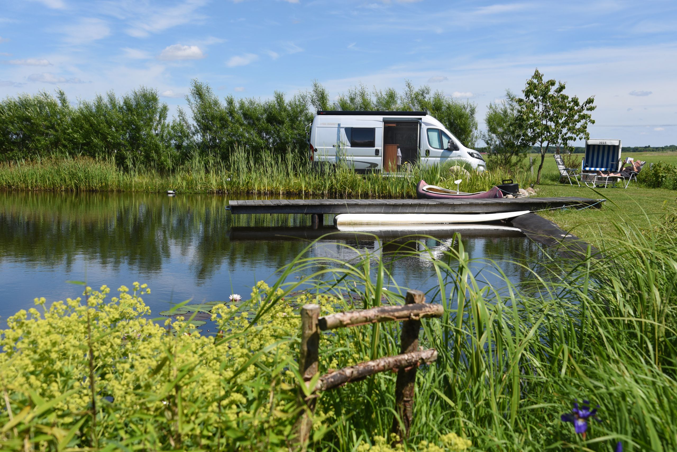 Wohnmobil steht an einem Badeteich inmitten einer idyllischen Wiesenlandschaft.