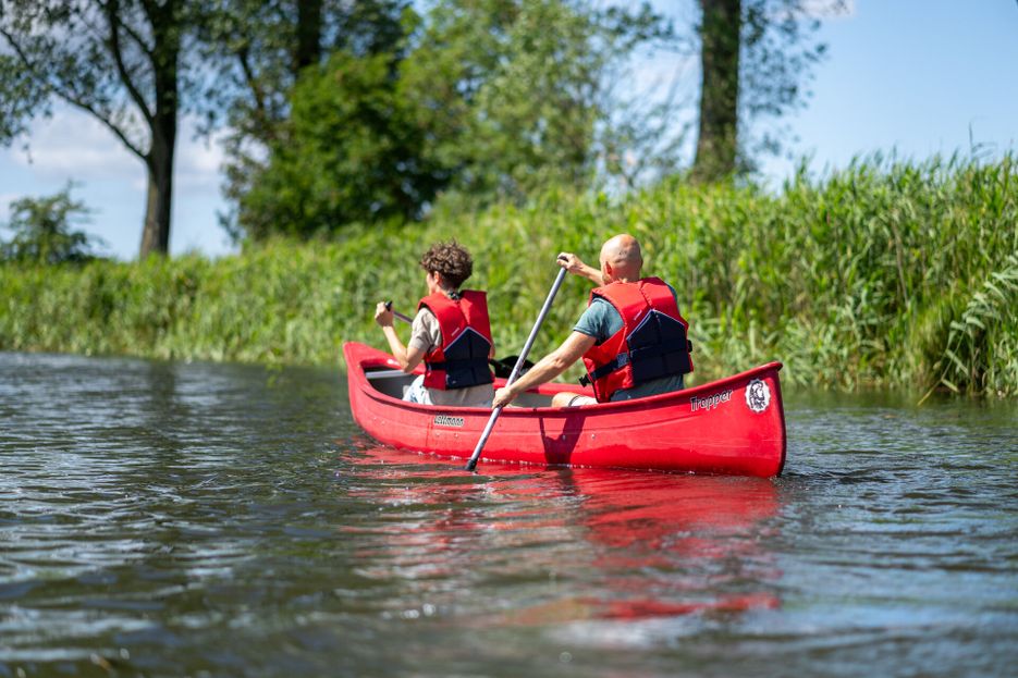 Ein Paar sitzt in einem roten Kanu und paddelt auf einem schmalen Fluss.