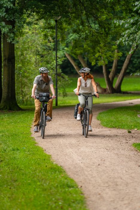 Paar genießt eine Fahrradtour im Grünen und fährt durch den Kurpark in Bad Bramstedt.